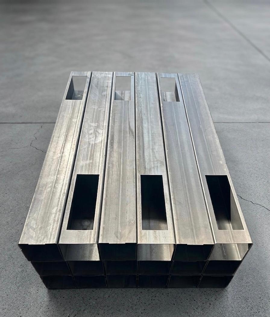 Bundle of precision-cut square steel tubes with rectangular slot cutouts, stacked on a workshop floor
